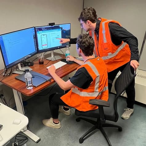 Two teammates in safety vests working at a monitor
